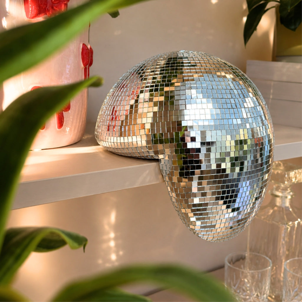 Smeltet disco ball dekor på hylle med speilrefleksjoner og varm belysning
