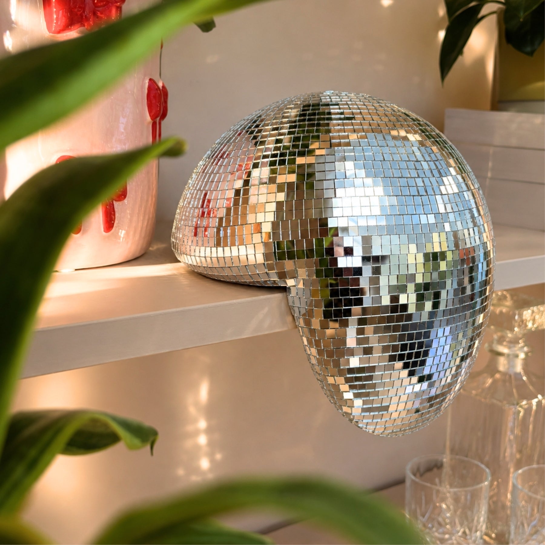 Smeltet disco ball dekor på hylle med speilrefleksjoner og varm belysning