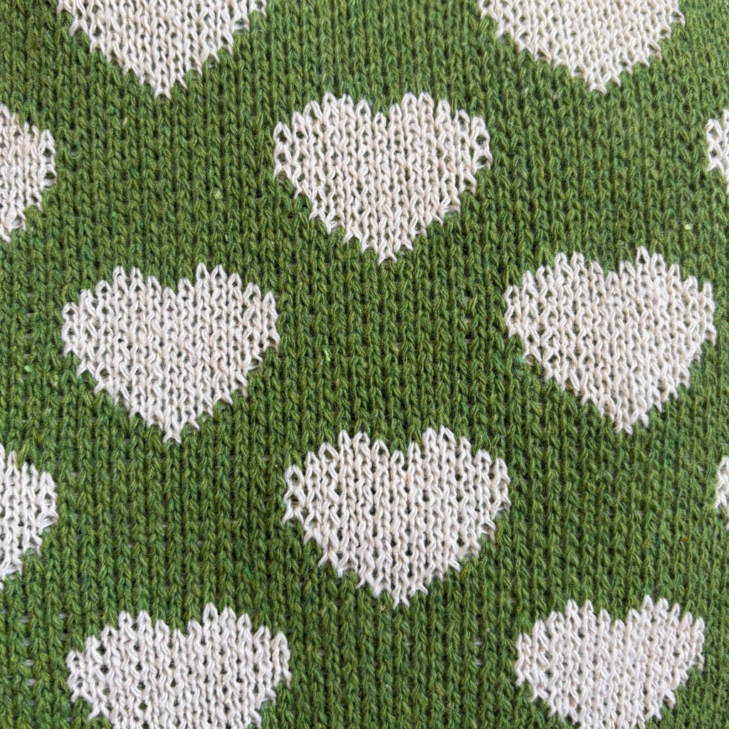 Nærbilde av grønn strikket totebag som viser tekstur og detaljer i hjertemønsteret.