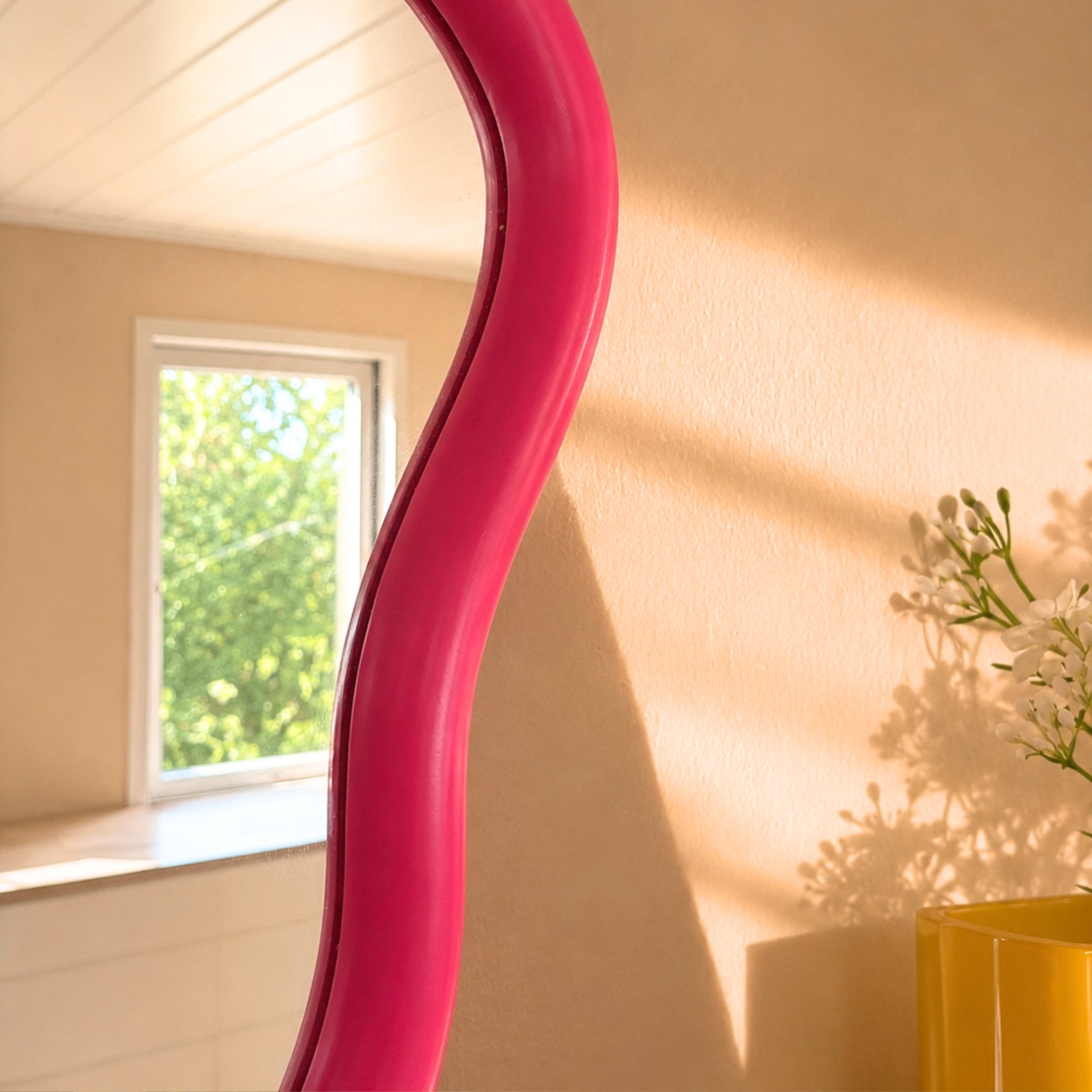 Detaljbilde av rosa organisk speilramme med refleksjon av vindu og grønn natur i naturlig dagslys.