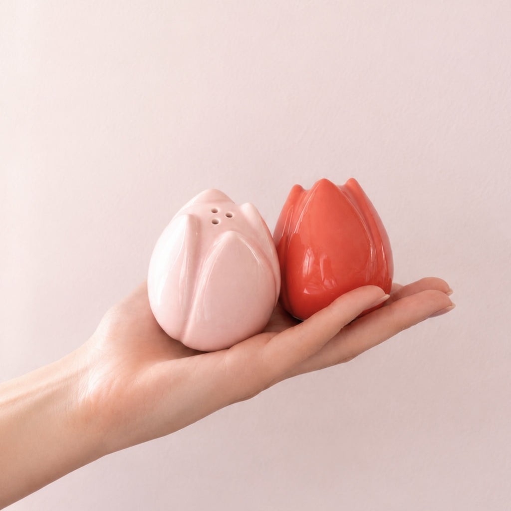 Tulipanformede salt- og pepperbøsser i rosa og korall holdt i hånd mot lys rosa vegg.