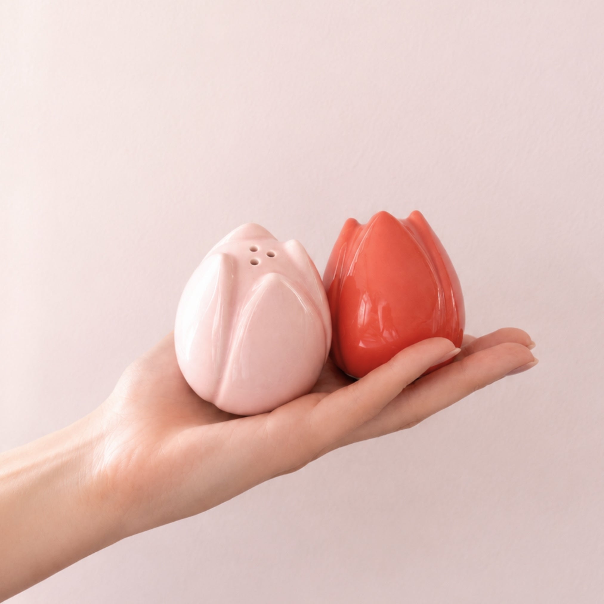 Tulipanformede salt- og pepperbøsser i rosa og korall holdt i hånd mot lys rosa vegg.